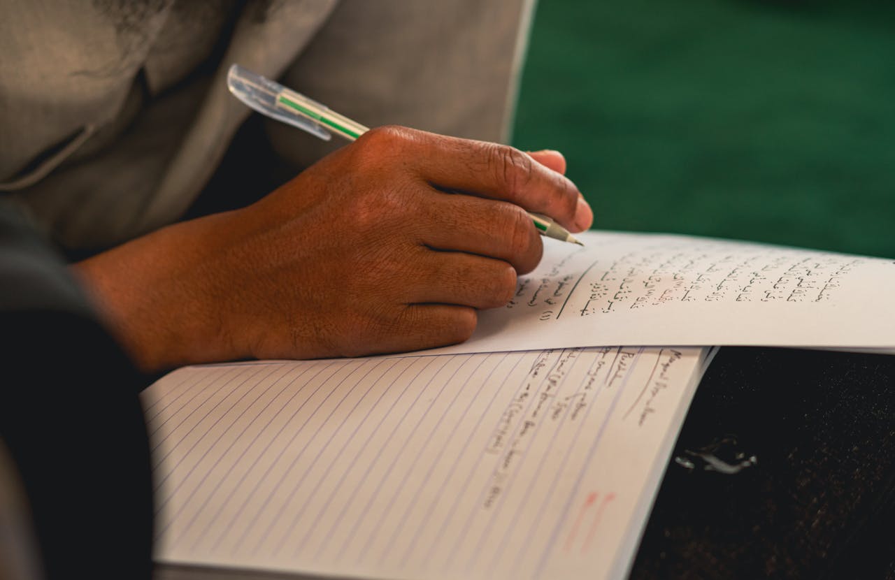 Detailed view of a persons hand writing with a pen on paper in Arabic script.