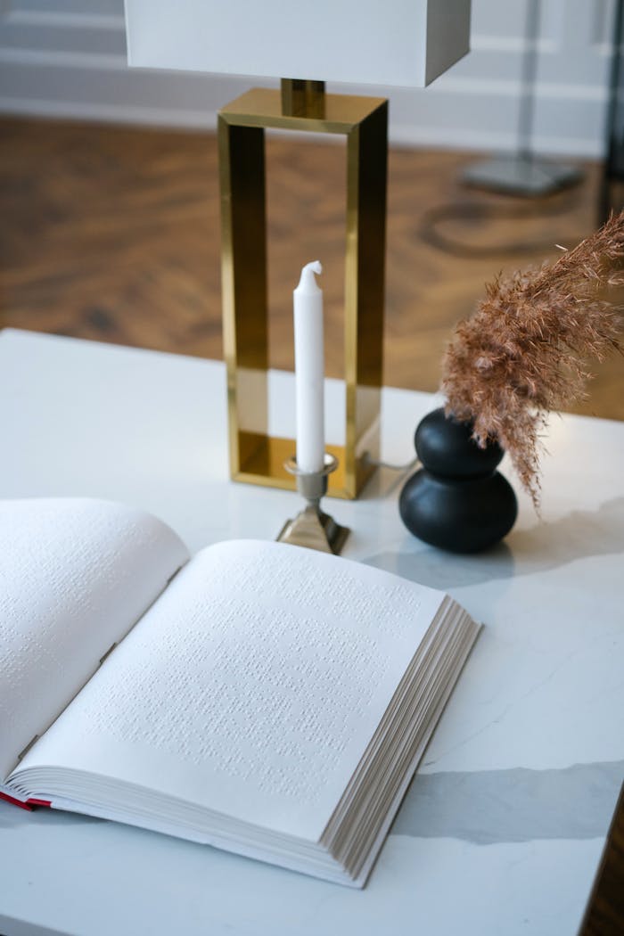 A braille book on a table with a candle, lamp, and decor in a cozy interior.